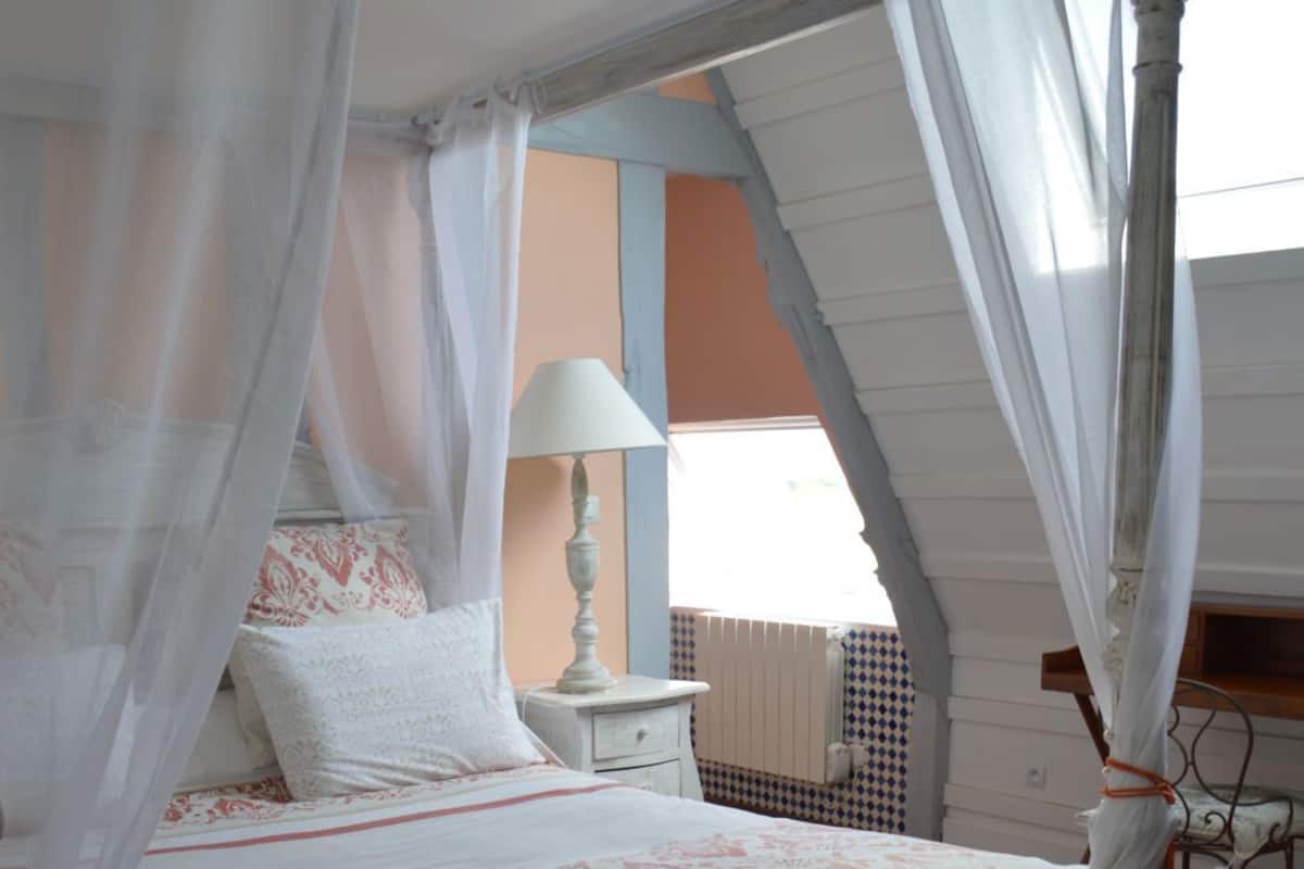 A bedroom with a canopy bed, a bedside table with a lamp, and a tray with cups and glasses.