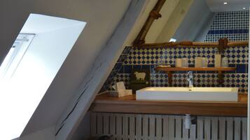 Une salle de bain avec un plafond en pente, un meuble-lavabo en bois, un miroir et un pare-feu en carrelage.