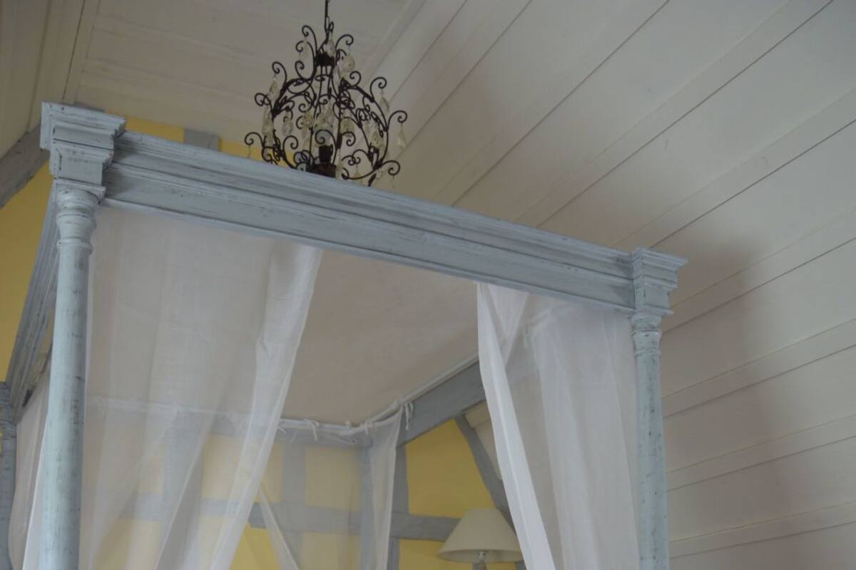 A four-poster bed with a canopy, a bedside table, a chair, and a patterned rug.
