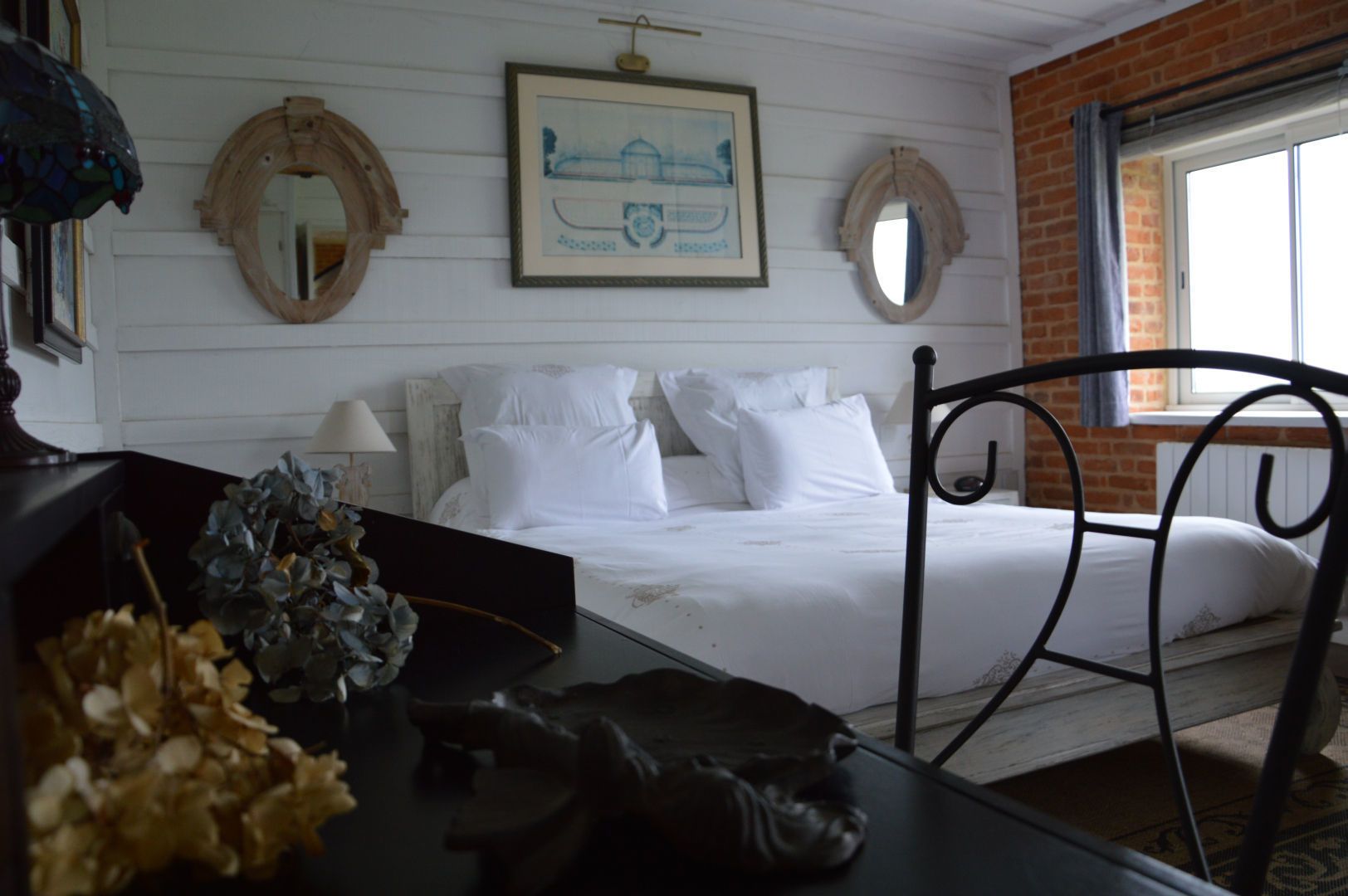 A bedroom with a bed, a desk, and a chair. There are two framed pictures on the wall and a window with a view of the outside.