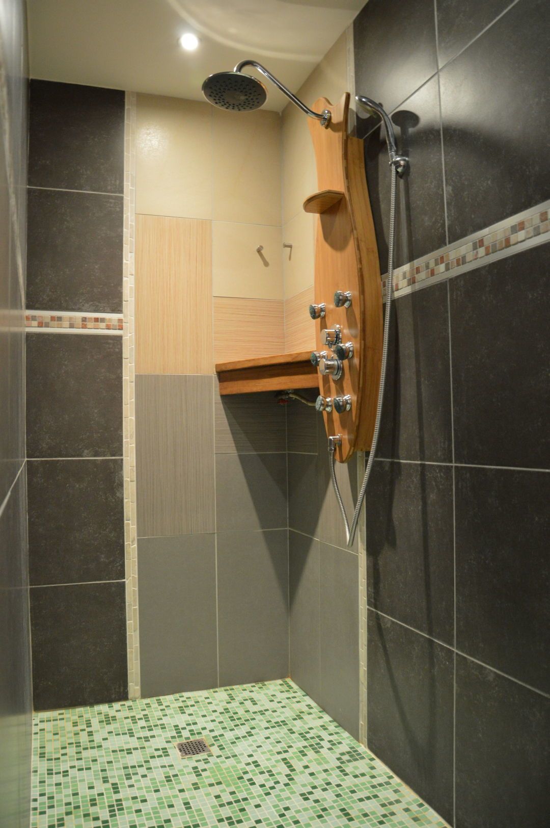 Een douche met een handdouche, een houten plank en een betegelde vloer.
