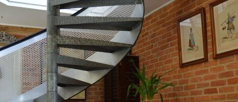 Una escalera de caracol con detalles metálicos, una mesita con sillas y una alfombra estampada.