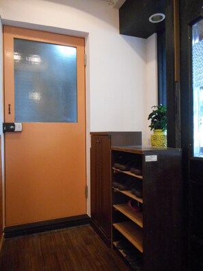 A hallway with a wooden door, a shoe rack, and a potted plant.
