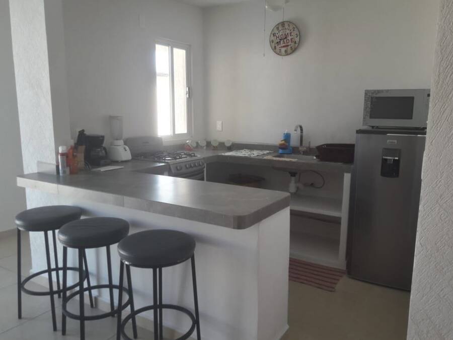 Una cocina moderna con una isla central, taburetes de bar, un refrigerador y un microondas.