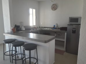 A modern kitchen with a central island, bar stools, a refrigerator, and a microwave. - Refugio Diamante (Acapulco)