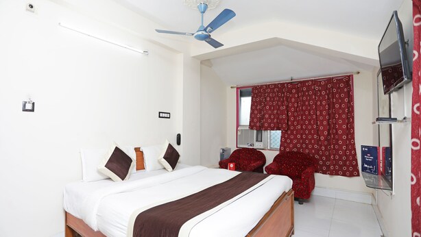 A bedroom with a bed, a ceiling fan, a red curtain, a TV, and a small table with chairs. - OYO 11631 Star Inn (Bhubaneshwar)