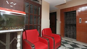 A lobby with a fish tank, two red chairs, a tiled floor, and a door with a metal gate. - OYO 11631 Star Inn (Bhubaneshwar)