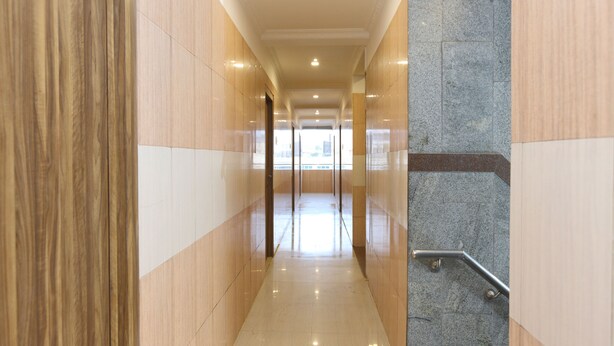 Un pasillo moderno y bien iluminado, con piso pulido, paredes de madera y piedra, y una barandilla a la derecha.