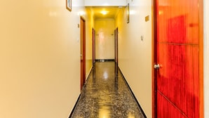 Un pasillo de hotel con piso de mármol, paredes amarillas y una puerta roja a la derecha.