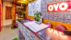 Zona de recepción con mostrador, estatua de Buda, pared con cartel 'RECEPTION OYO' y un diseño decorativo en la pared.