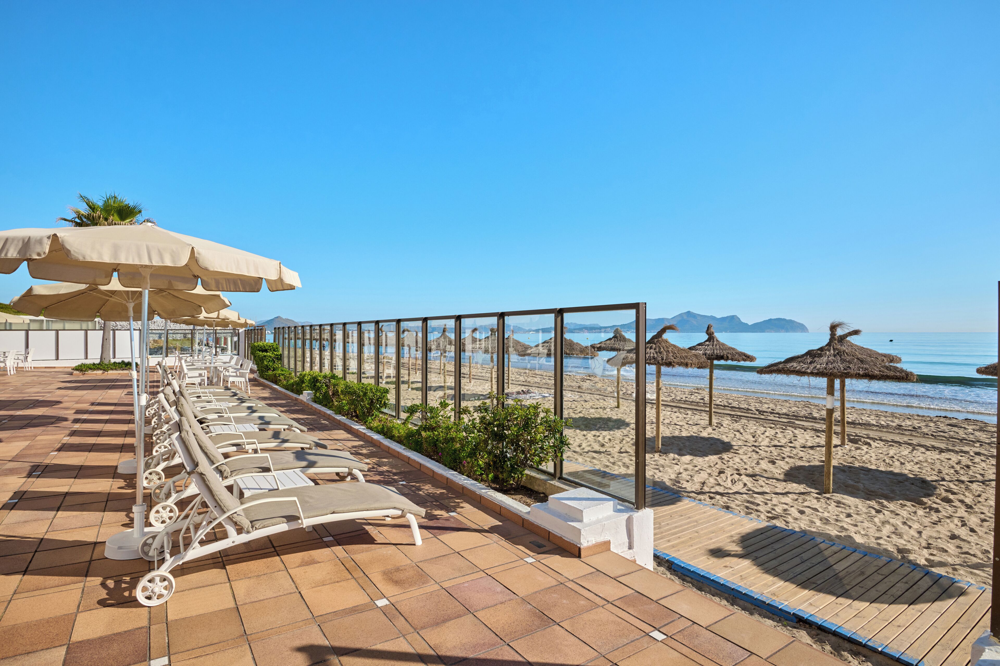 Een terras aan het strand met ligbedden, parasols en uitzicht op het strand en de oceaan.