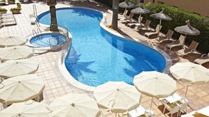 A swimming pool with sun loungers and umbrellas, surrounded by a tiled deck.