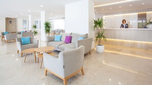A modern hotel lobby with a reception desk, seating area with sofas and chairs, and potted plants.