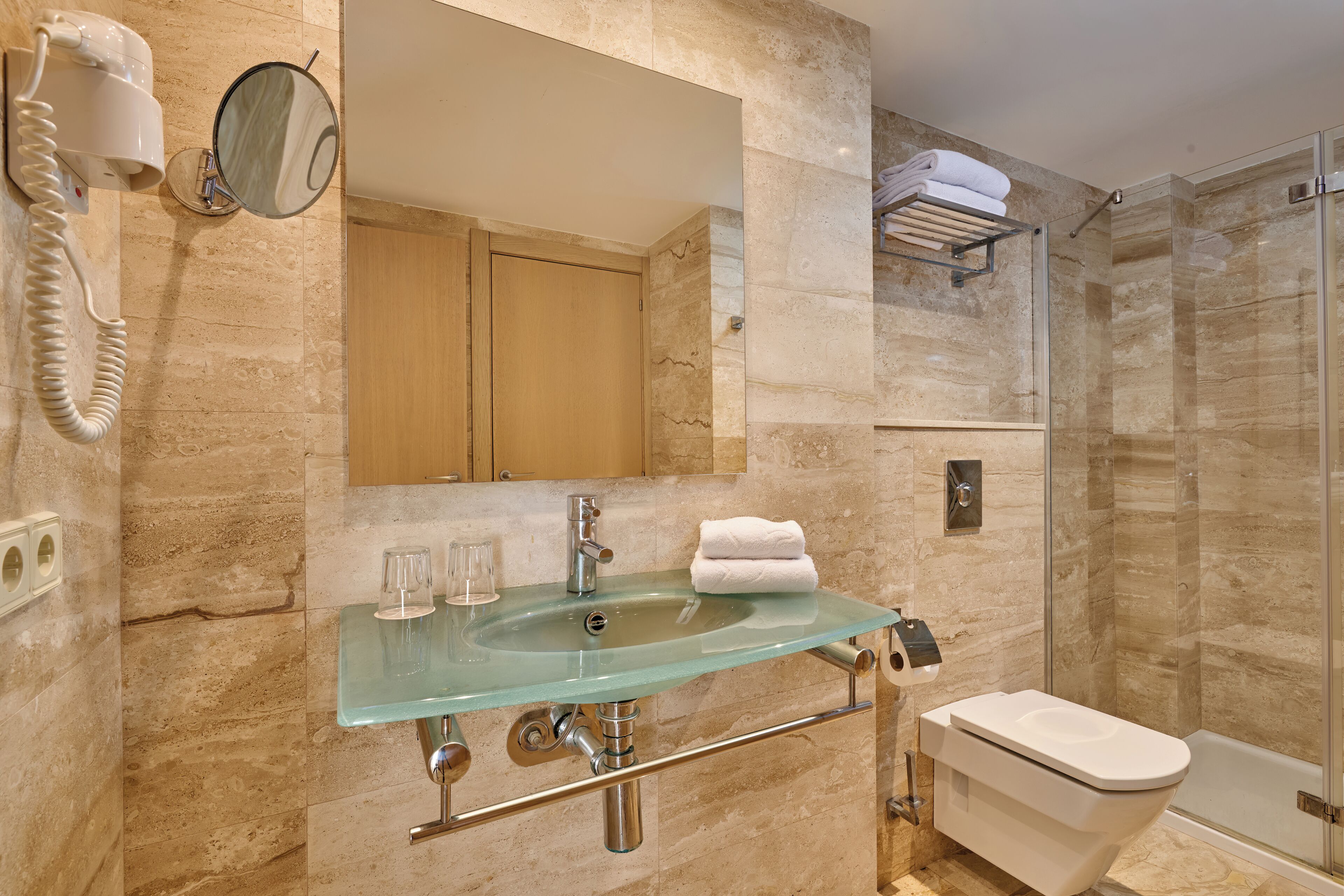 Un baño con lavamanos de vidrio, inodoro, ducha y espejo.