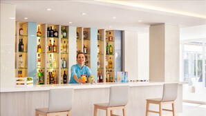 A bar area with a bartender, shelves of various liquor bottles, and two bar stools.