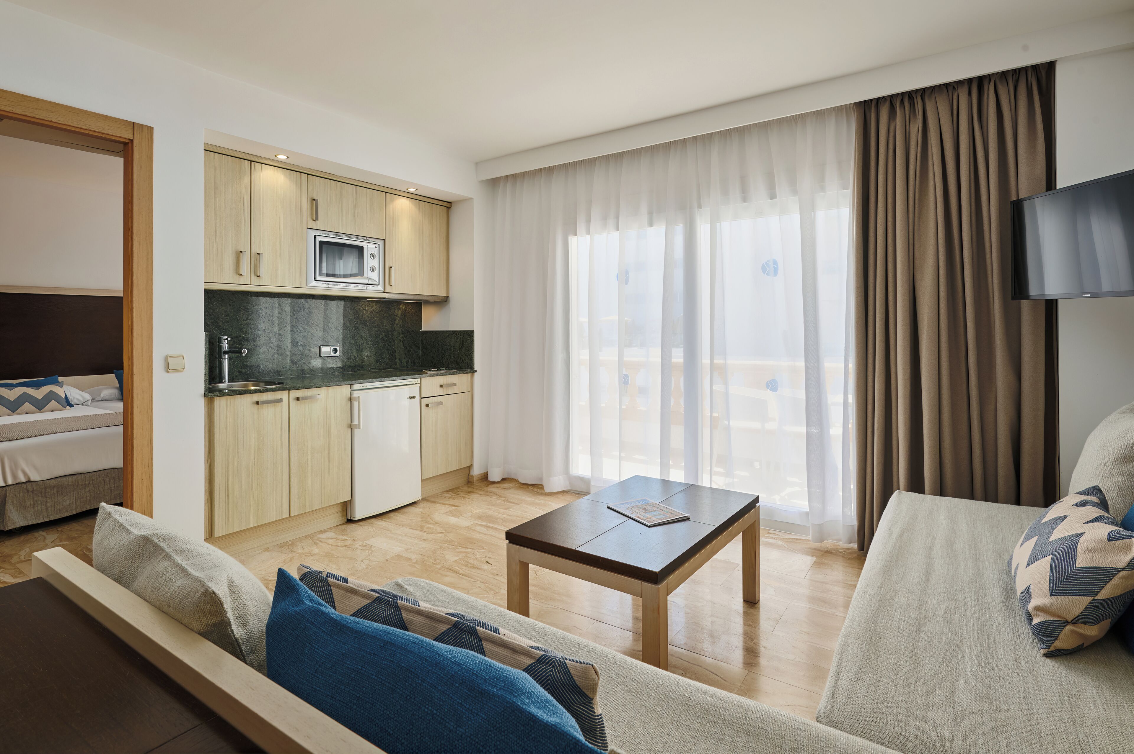 Een moderne hotelkamer met een kitchenette, een bank, een bijzettafeltje en een televisie.
