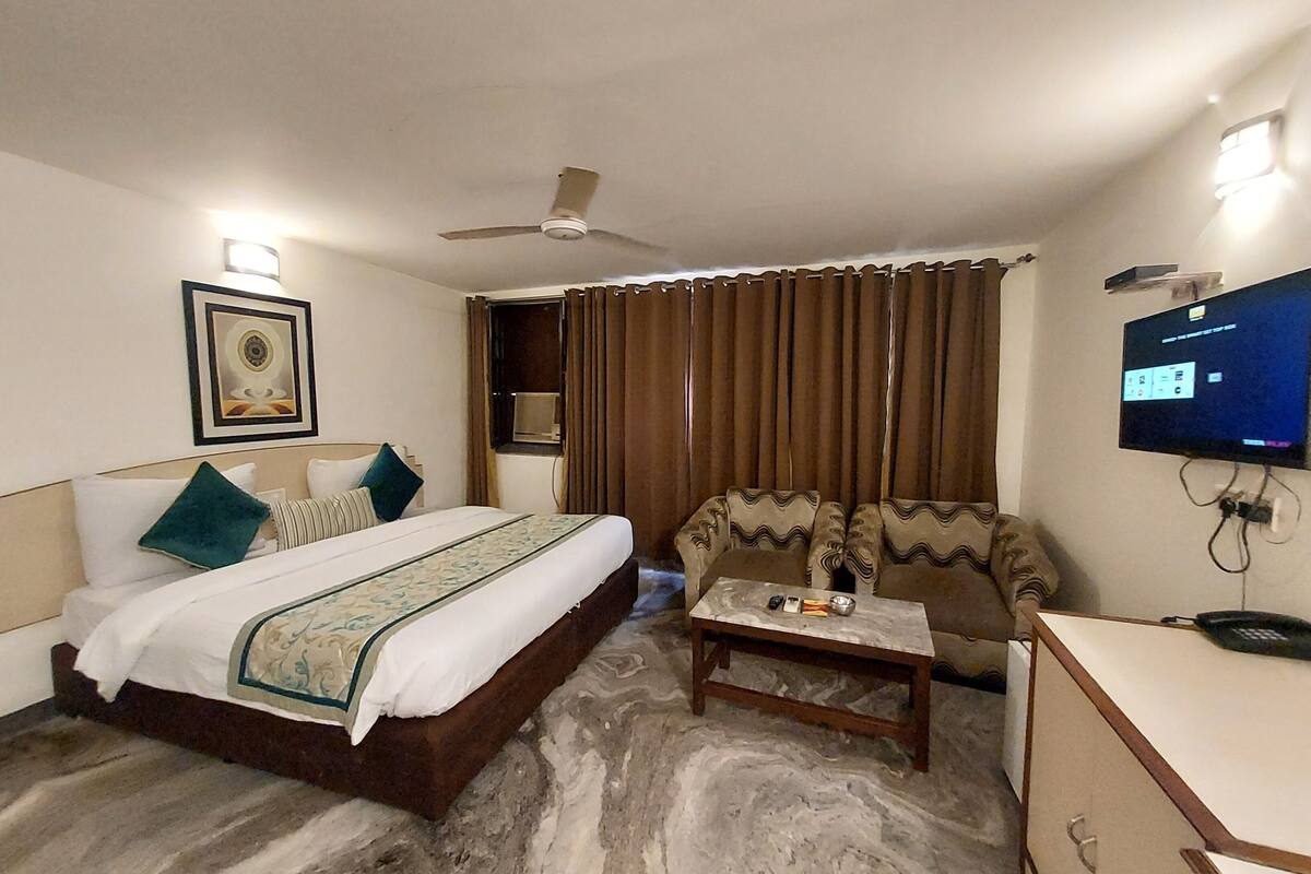A hotel room with a bed, a sofa, a television, a ceiling fan, and a window with curtains.