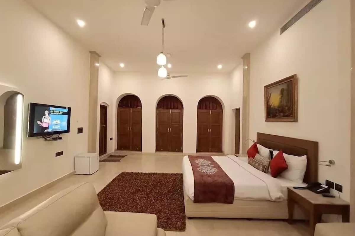 A hotel room with a bed, a TV, a ceiling fan, and a painting on the wall.