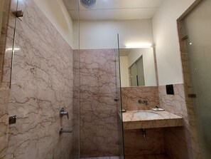 A modern bathroom with marble walls, a glass shower enclosure, and a sink with a mirror above it. - Hotel Green Castle (Heritage Hotel) (New Delhi)