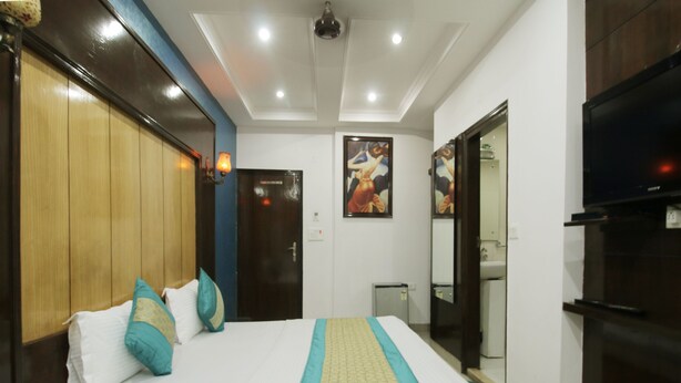 Una habitación de hotel con cama, televisión, baño e iluminación en el techo.