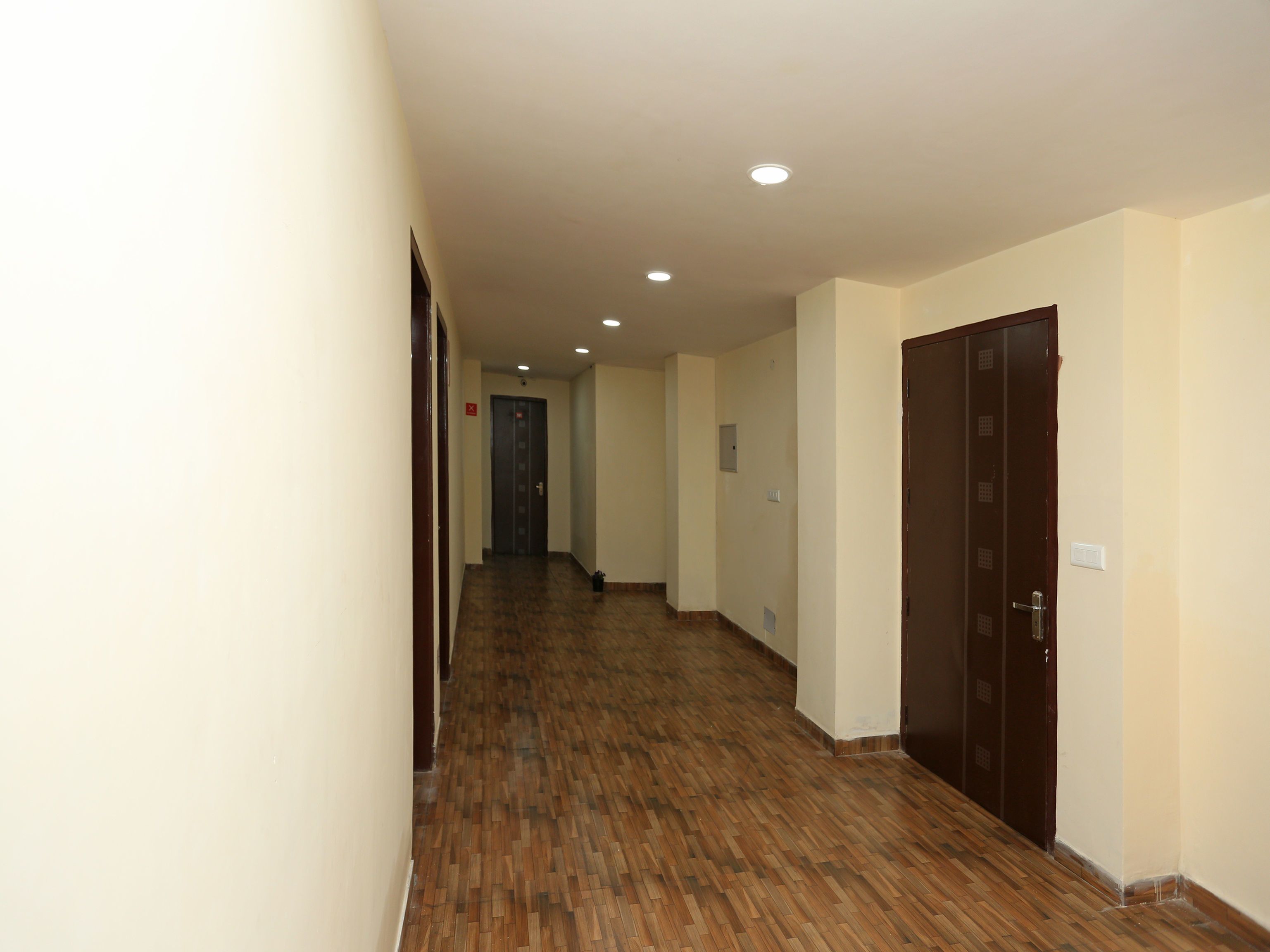 A hallway with wooden flooring, cream-colored walls, and a door at the end.