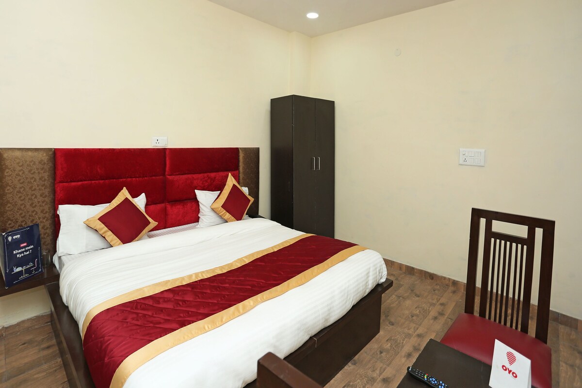 A hotel room with a large bed, a wardrobe, a desk with a chair, and a small table with a sign.