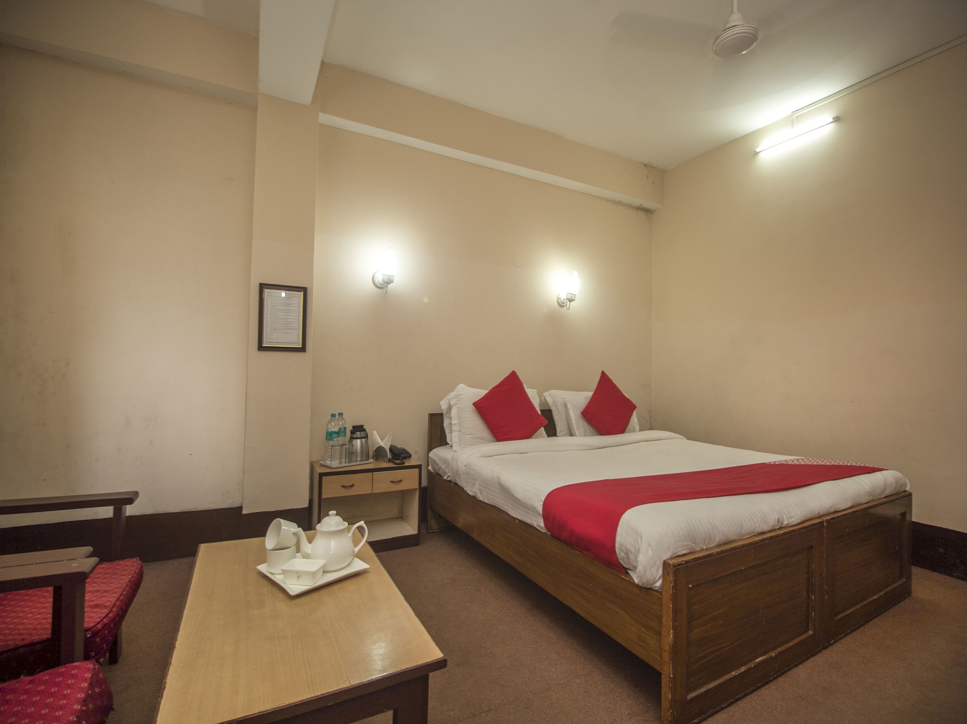 A hotel room with a single bed, a bedside table with a teapot and cups, a nightstand, and a framed certificate on the wall.