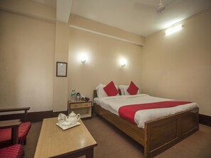 Una habitación de hotel con una cama individual, una mesita de noche con tetera y tazas, una lámpara y un diploma enmarcado en la pared.