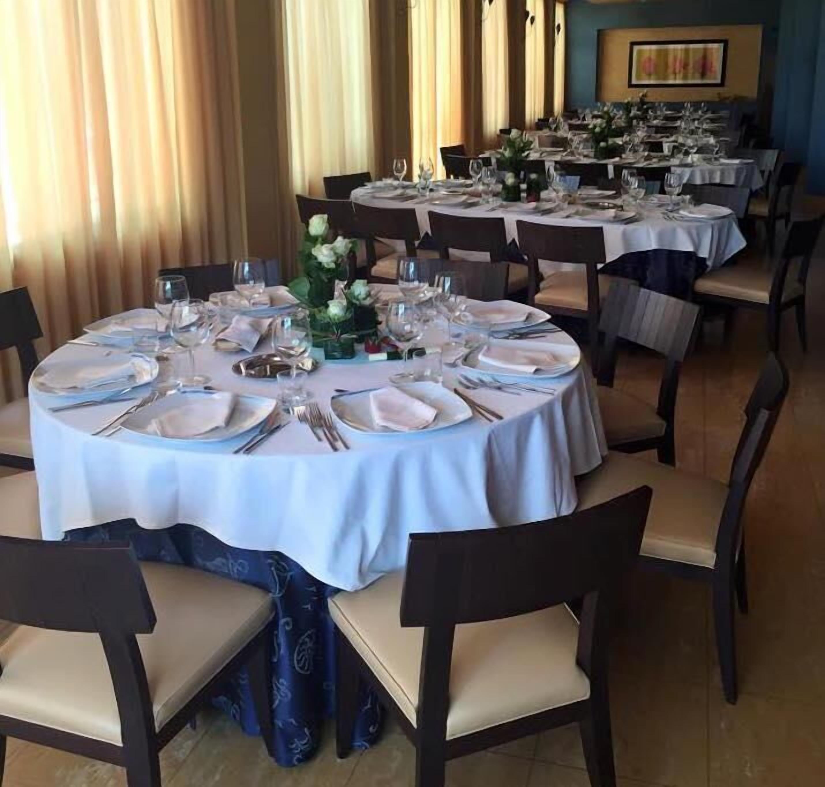 A restaurant with round tables set for dining, featuring white tablecloths and dark chairs.