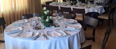 A restaurant with round tables set for dining, featuring white tablecloths and dark chairs.