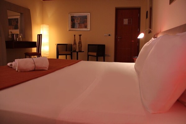 A hotel room with a bed, a chair, a table, a lamp, and a door. - Meridian Hotel (Guardia Piemontese)