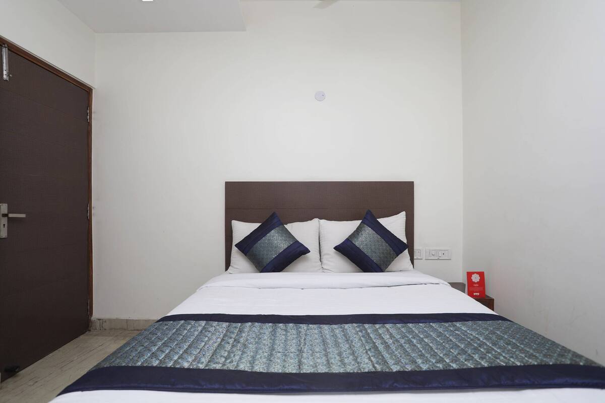 Een hotelkamer met een bed, een houten deur, een nachtkastje en een rood voorwerp op het nachtkastje.