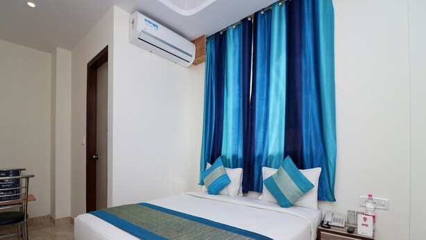 Una habitación de hotel con cama, mesita de noche, escritorio, equipo de aire acondicionado y cortina.
