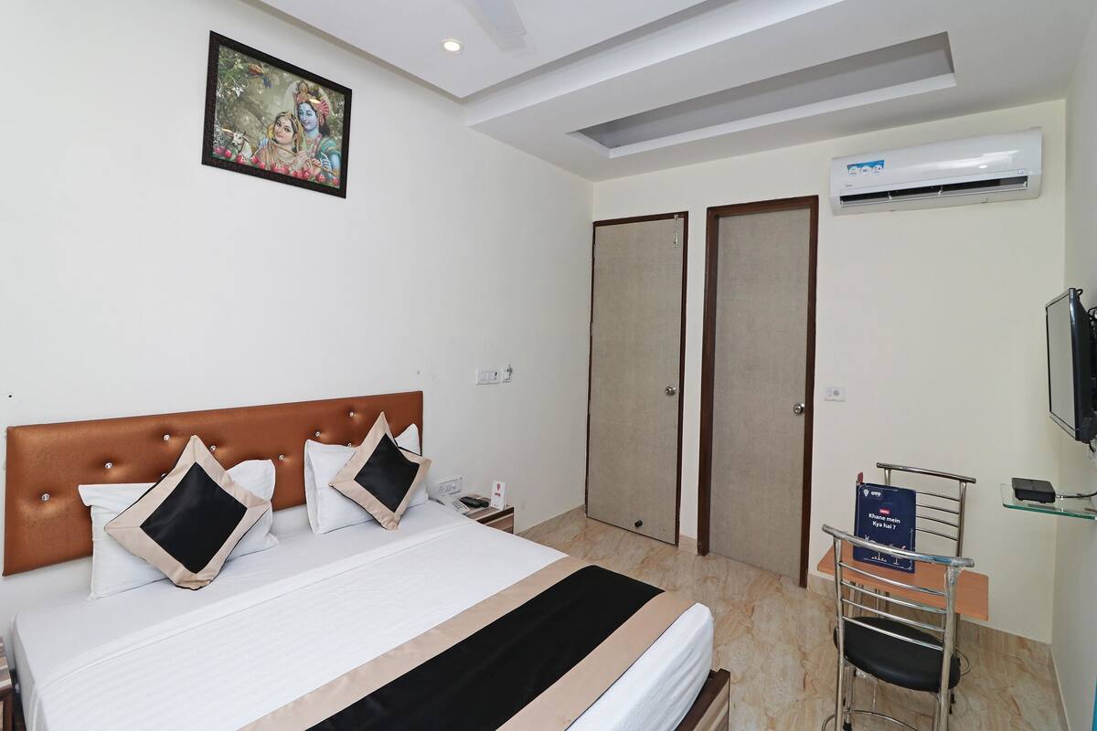 A hotel room with a bed, a ceiling fan, an air conditioning unit, a television, and a desk with a chair.