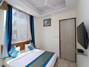 A hotel room with a bed, a television, a door, and a window with curtains. - OYO 12754 Hotel The Best (New Delhi)