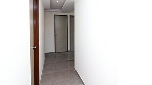 Un pasillo con una puerta de madera a la izquierda, una pared blanca y una puerta con el número 205.