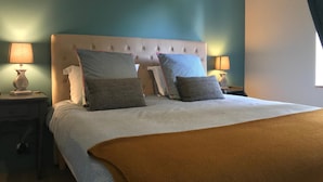 A neatly made bed with a tufted headboard, two bedside lamps, and a window with curtains. - A La Lettre Thé (Valencisse)