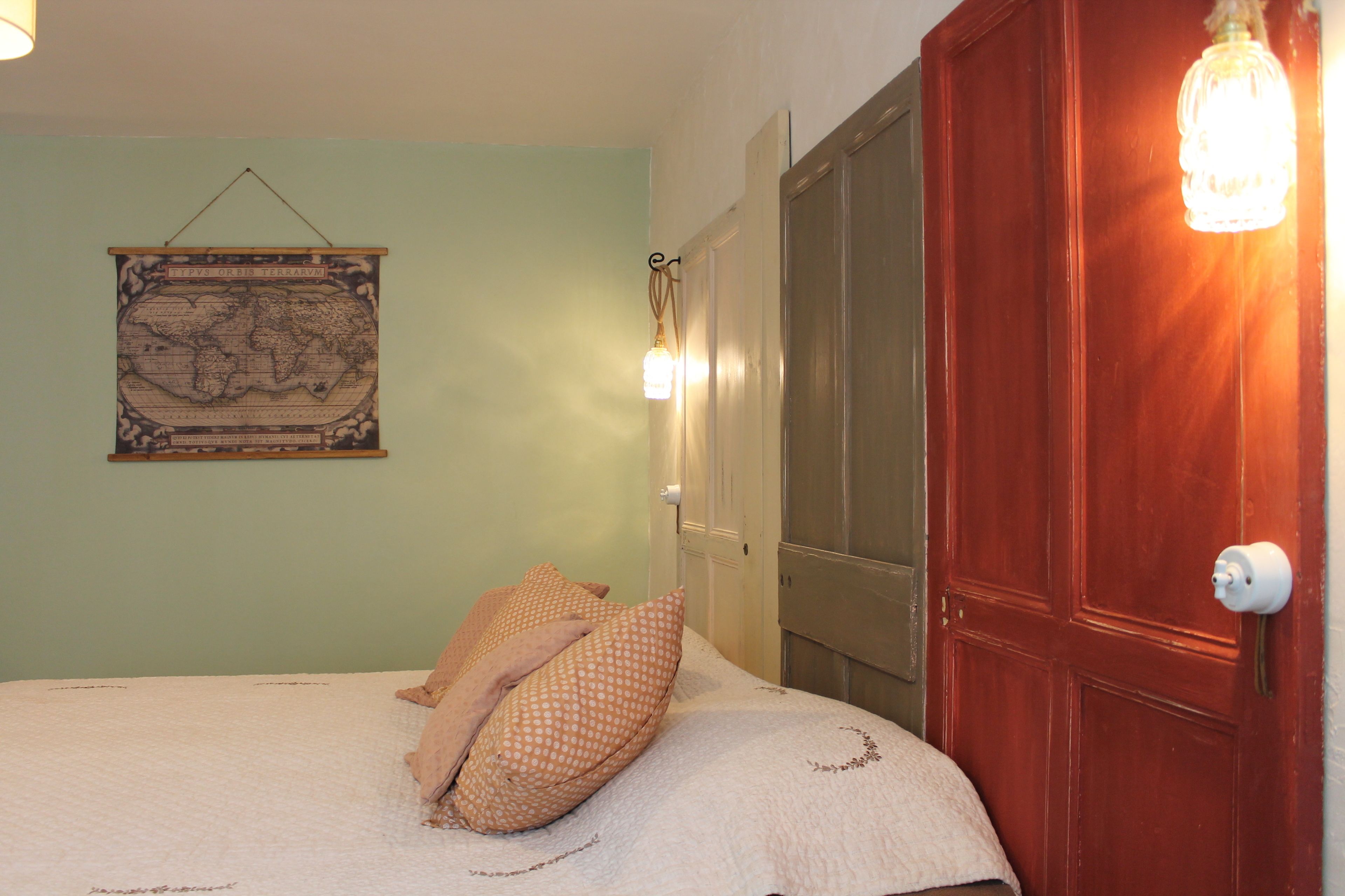 Une chambre à coucher avec un lit, des oreillers, une carte accrochée au mur et une porte en bois.
