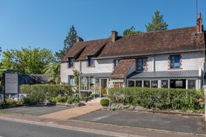 A two-story building with a traditional brick facade, a covered entrance, and a small garden area with potted plants. - A La Lettre Thé (Valencisse)