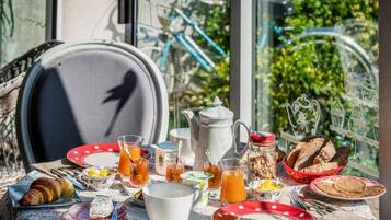 Une table dressée pour le petit-déjeuner, avec un croissant, du thé et du pain, et en toile de fond, une vue sur la verdure et des vélos à l'extérieur.