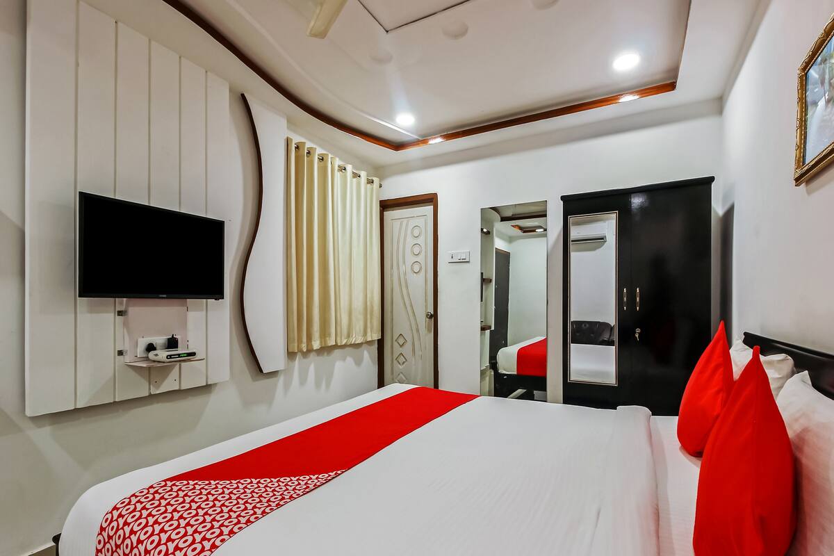 A hotel room with a large bed, a flat-screen TV mounted on the wall, a wardrobe, and a mirror.
