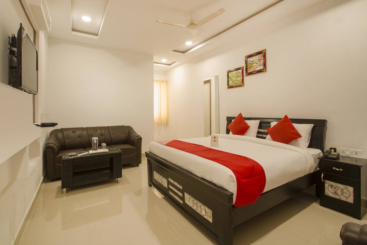 A modern hotel room with a large bed, a sofa, a TV, and a ceiling fan.