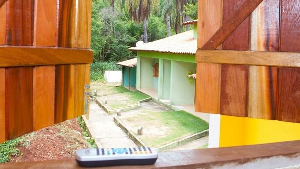 Vista a través de puertas de madera de un patio con un edificio verde, palmeras y un control remoto sobre una mesa.