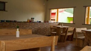 Un comedor rústico con mesas y sillas de madera, pared de ladrillo y ventana con vistas a un edificio verde.