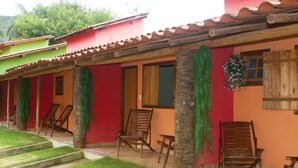 Un edificio de fachada roja, puertas de madera y tejado de tejas. Hay sillas de madera y un banco en el exterior.