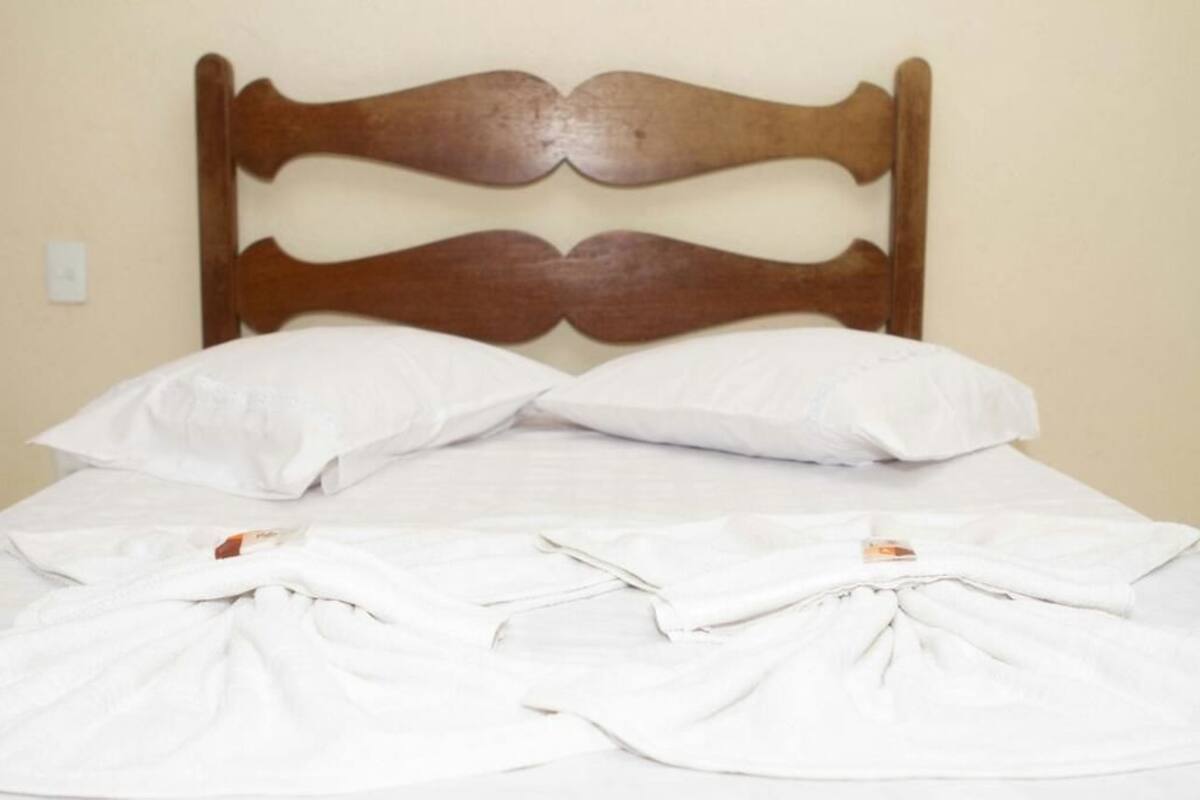 Un lit avec une tête de lit en bois, une literie blanche et deux oreillers blancs.