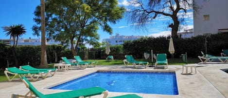 Zona de piscina con múltiples sillas reclinables verdes y una piscina pequeña.