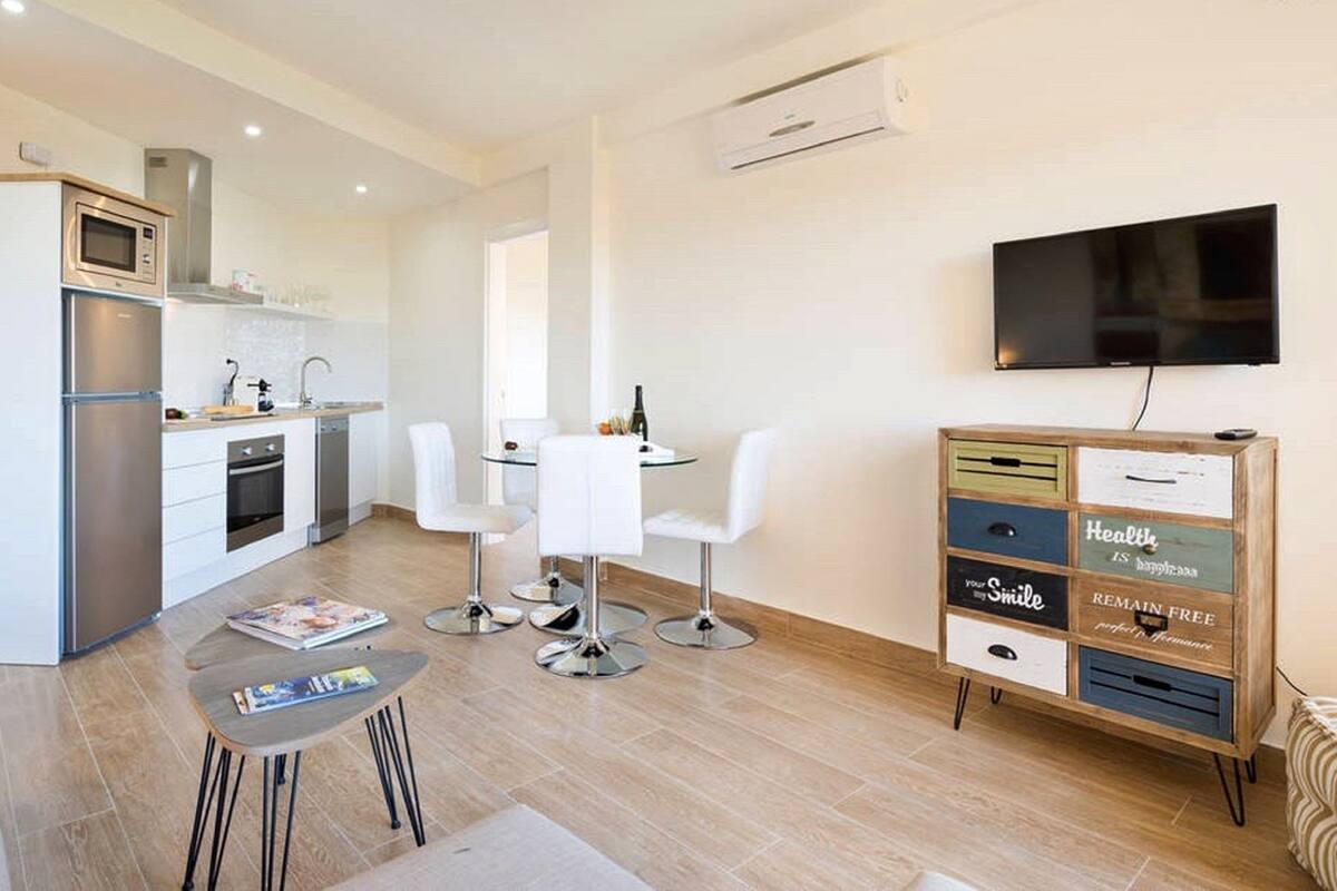 A compact kitchen with a microwave, oven, and sink, a dining area with a table and chairs, and a TV mounted on the wall.