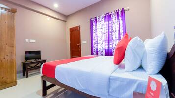 A hotel room with a bed, a TV, a wooden wardrobe, and purple curtains.