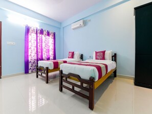 A hotel room with two beds, a window with purple curtains, an air conditioning unit, and a black wardrobe.